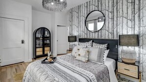 Une chambre à coucher avec un grand lit, un miroir rond, une tête de lit noire et une table de chevet avec une lampe.