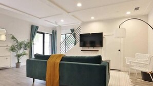 Ein modernes Wohnzimmer mit einer Couch, einem Fernseher, einer Treppe und einer Pflanze.