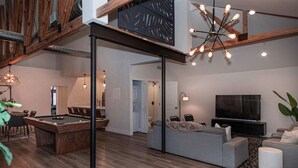 Ein modernes Wohnzimmer mit Billardtisch, einer Couch, einem Fernseher und einer Deckenleuchte.