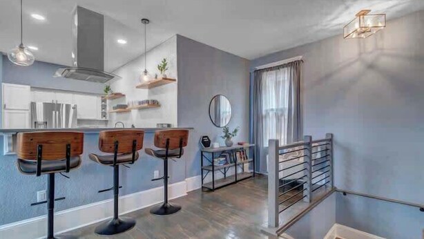 A modern kitchen with bar stools, a dining area with a mirror, and a staircase with a railing. - Gigantic duplex in Springfield (Jacksonville)