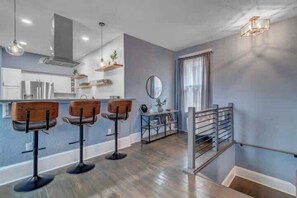 A modern kitchen with bar stools, a dining area with a mirror, and a staircase with a railing. - Gigantic duplex in Springfield (Jacksonville)