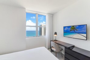 A hotel room with a large window, a desk with a chair, a bed, and a TV on the wall.
