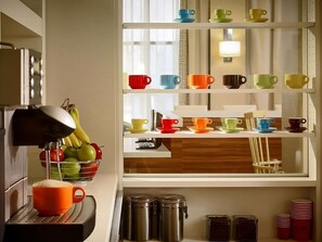 Una cocina con frutero, cafetera y repisas con tazas y recipientes de colores.