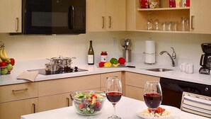Una cocina moderna con microondas, estufa y diversos utensilios de cocina. Hay dos vasos de vino tinto y un bol de ensalada sobre la encimera.