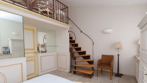 A bedroom with a bed, a chair, a lamp, a staircase, and a mirror.