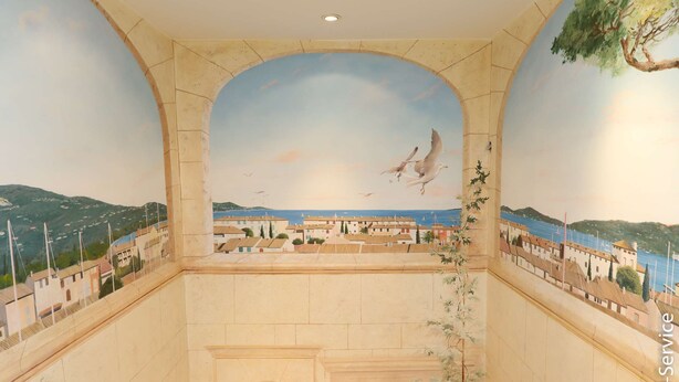 A room with a mural of a coastal town and seagulls, a tiled floor, and a potted plant.