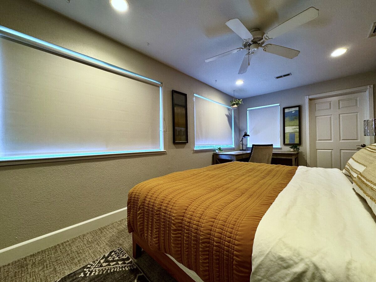 Ett sovrum med en säng, ett skrivbord, en stol, en takfläkt och en dörr.
