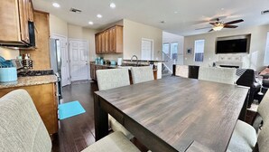 Un'ampia sala da pranzo con un grande tavolo in legno e numerosi posti a sedere, una cucina con mobili in legno e una ventola a soffitto.