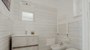 A bathroom with a modern design, featuring a large mirror, a sink with a cabinet, a bidet, and a toilet.