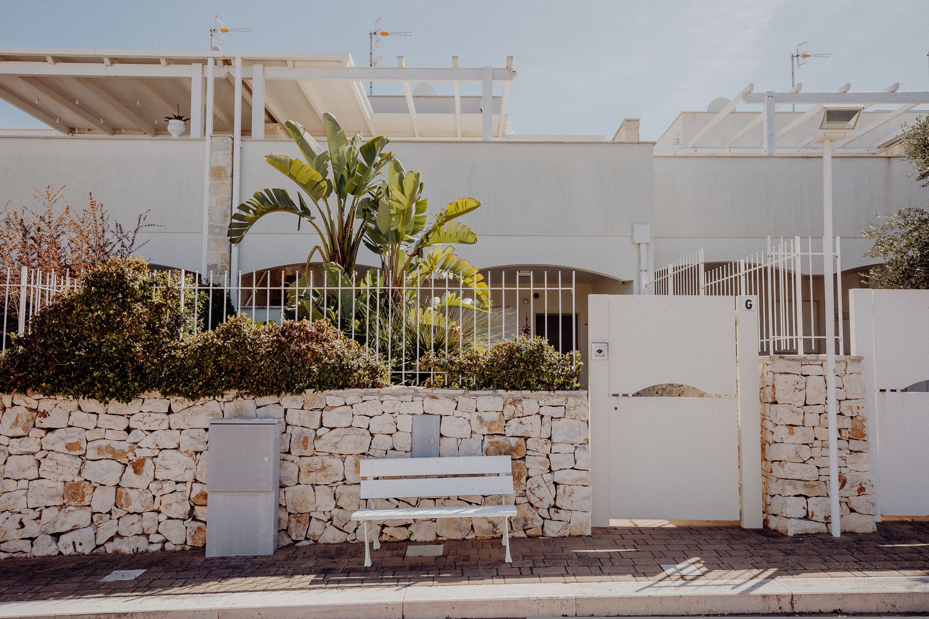 A stone wall, a white bench, and a gated entrance to a building.