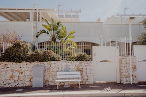 A stone wall, a white bench, and a gated entrance to a building.