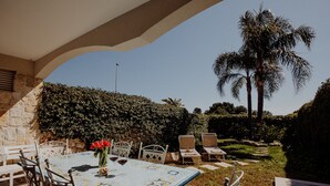 An outdoor patio with a table set for dining, surrounded by chairs, and a view of a palm tree and garden.