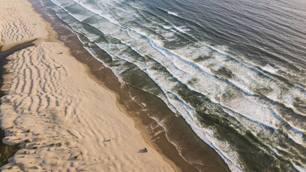 A beach with waves approaching the shore, sandy beach, and footprints.