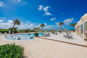 Zona de piscina en un resort, con sillones de descanso y sombrillas, rodeada de palmeras y un cielo despejado.