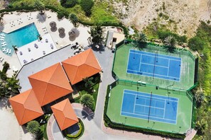 An aerial view of a resort with a swimming pool, tennis courts, and a building with a distinctive orange roof.