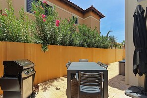 An outdoor patio with a barbecue grill, a table, and chairs.