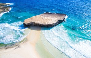 Una playa con una gran formación rocosa rodeada de aguas azules cristalinas y una orilla arenosa.