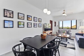 A modern living room with a dining area, large windows, and a ceiling fan.