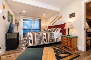 A bedroom with a bed, a wooden dresser, a television, and a window with a view. - Water's Edge Retreat (Waverly)