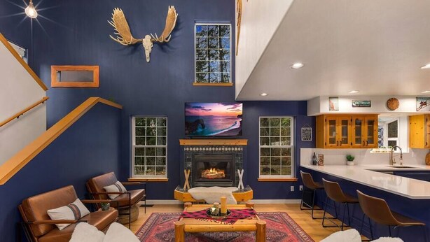 A modern living room with a fireplace, seating area, and a kitchen with bar seating. - Sandpoint Mountain Retreat (Bonner County)
