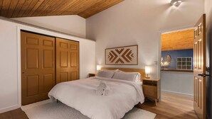 A bedroom with a large bed, wooden ceiling, and a wall-mounted artwork. - Sandpoint Mountain Retreat (Bonner County)