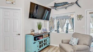 Una sala de estar con un mueble azul turquesa, un sofá color beige, un televisor de pantalla plana y una gran decoración de pez en la pared.