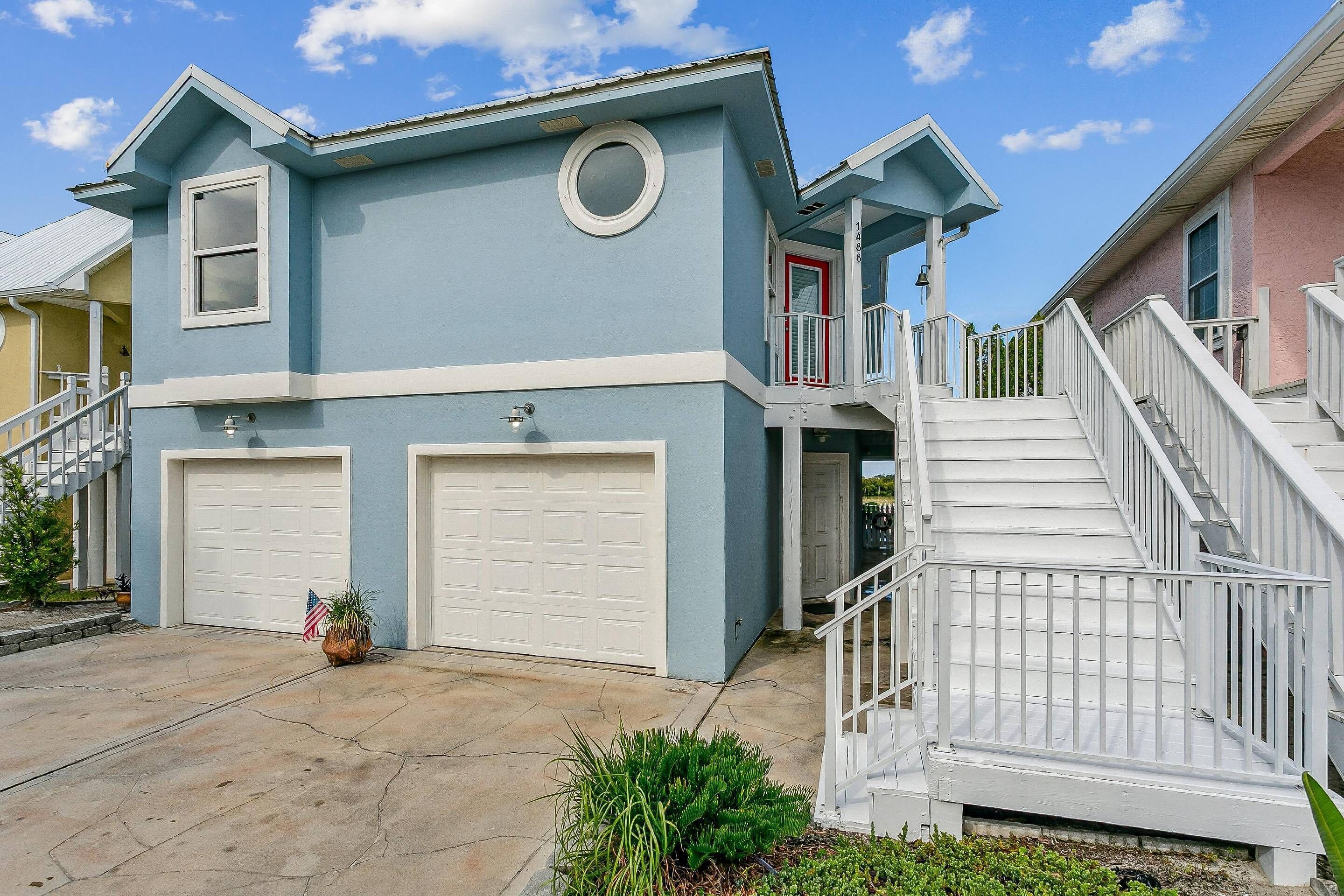 Une maison à deux étages, avec une façade bleue, des portes de garage blanches et un escalier blanc menant à un balcon.
