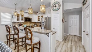 Una cocina con una isla central, luces colgantes y un reloj en la pared.