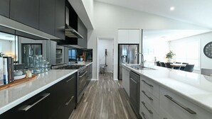 A modern kitchen with dark cabinetry, stainless steel appliances, and a large island with a sink. - Luxe on Lincoln - Close to Zoo, Rejuvenating Pool (Dubbo)