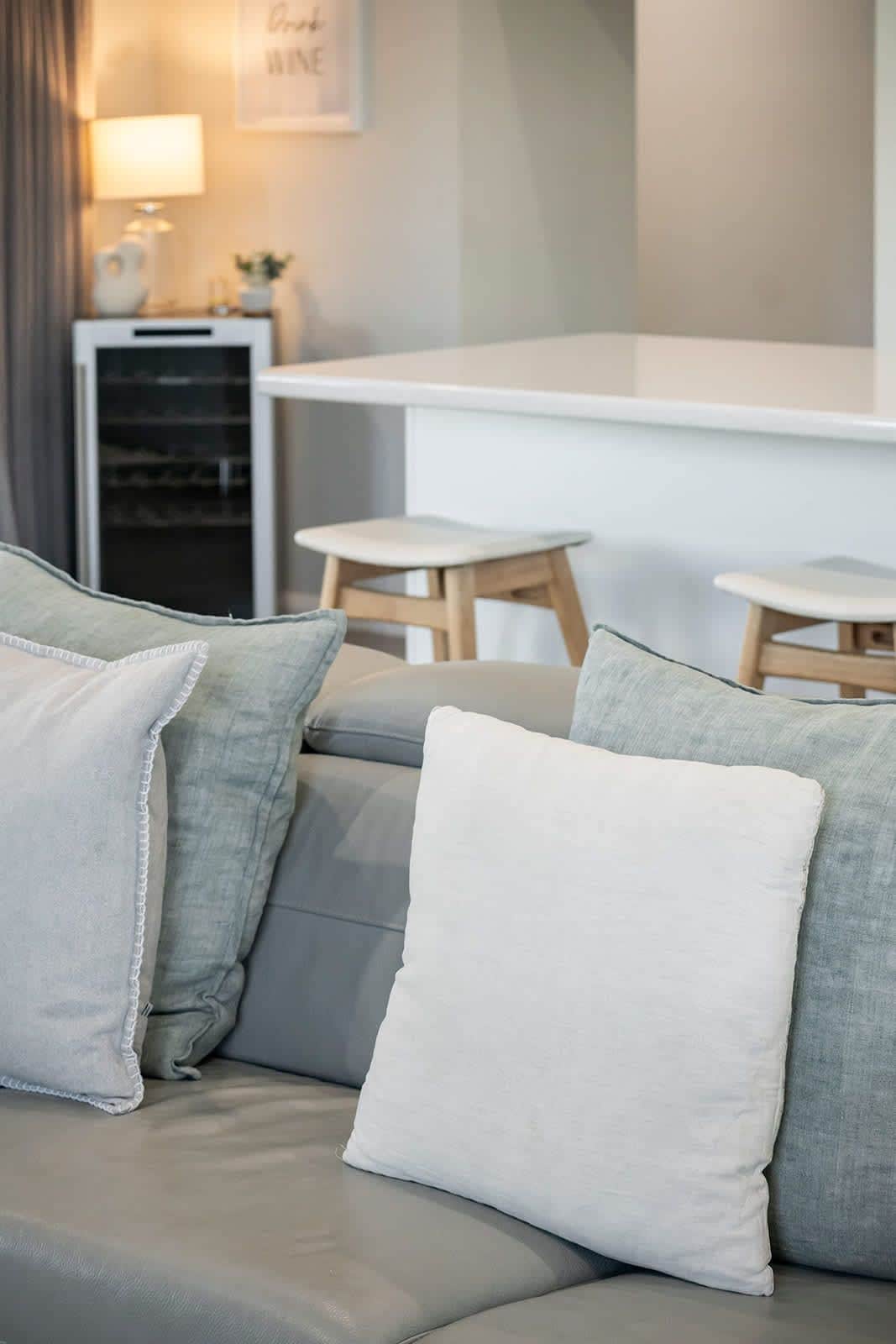 Un salon moderne avec un canapé gris, des coussins blancs et une petite table sur laquelle se trouve une lampe.