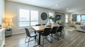 A modern living room with a dining area, large windows, and a flat-screen TV. - Luxe on Lincoln - Close to Zoo, Rejuvenating Pool (Dubbo)