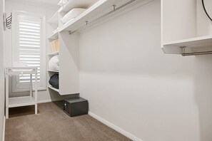 A walk-in closet with white shelving, a small table, and a shoe rack. - Luxe on Lincoln | A Honey Home (Dubbo)