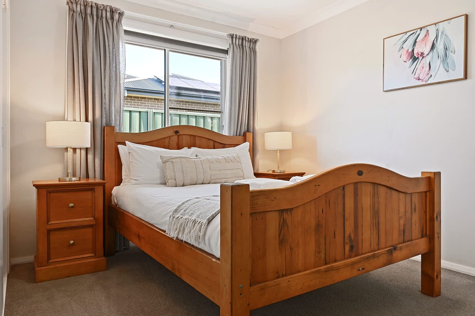 A wooden bed with a headboard, two bedside tables, and a window with curtains.