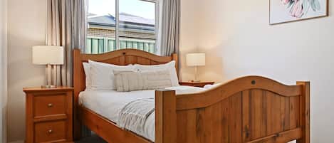 Una cama de madera con cabecera, dos mesitas de noche y una ventana con cortinas.