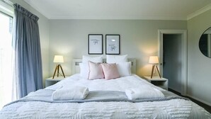 A neatly made bed with white bedding and pink pillows, two bedside lamps, and two framed pictures on the wall. - Luxe on Lincoln - Close to Zoo, Rejuvenating Pool (Dubbo)