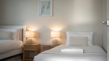 Ein Hotelzimmer mit zwei Betten, jeweils mit Nachttisch und Lampe. Darüber hängt ein gerahmtes Kunstwerk an der Wand.
