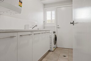 A laundry area with a washing machine, a sink, and cabinets. - Luxe on Lincoln | A Honey Home (Dubbo)