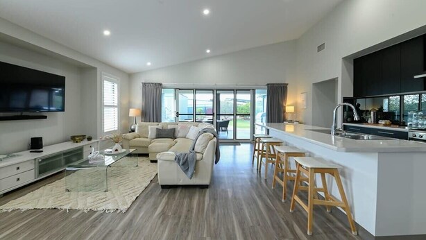 A modern kitchen with a large island, bar stools, and a dining area. - Luxe on Lincoln - Close to Zoo, Rejuvenating Pool (Dubbo)