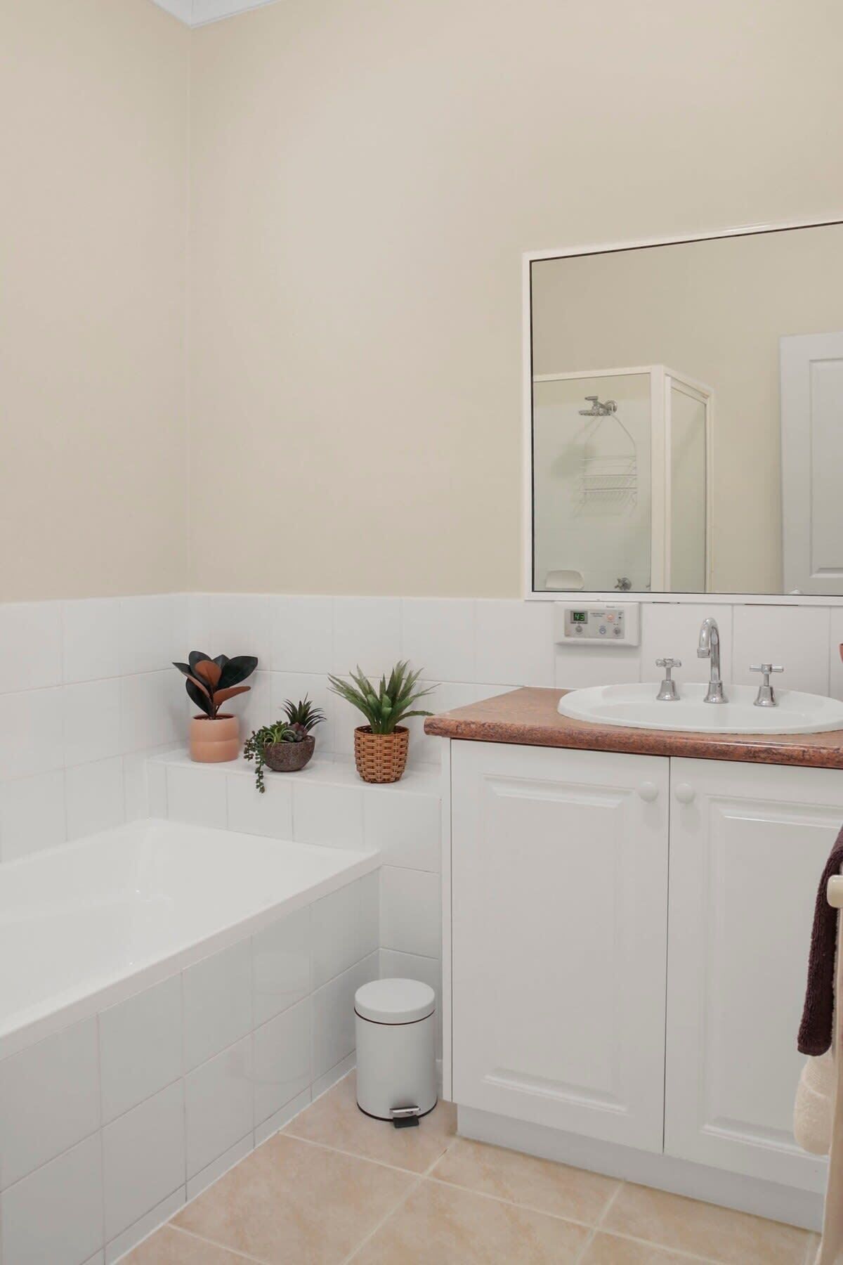 Un baño moderno con una bañera, un lavabo e inodoro. Hay plantas en macetas sobre el mueble del lavabo y un cubo de basura.
