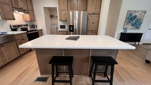 Een moderne keuken met houten kastjes, roestvrijstalen apparatuur en een marmeren eiland met twee krukken.