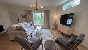 Een woonkamer met een bank, twee fauteuils, een salontafel, een televisie en een kroonluchter.