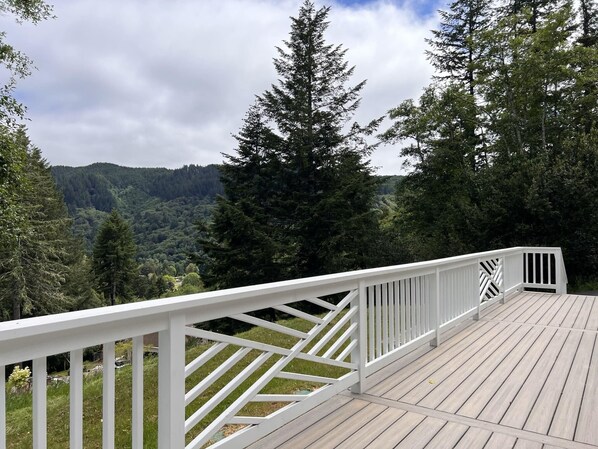 Une terrasse en bois, dotée de rampes blanches, qui offre une vue sur une colline boisée.