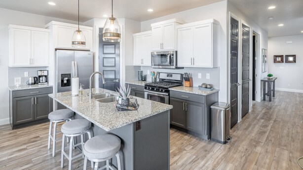A modern kitchen with granite countertops, stainless steel appliances, and a central island with bar stools. - Desert Skies (St. George)