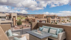 A balcony with outdoor furniture, a fire feature, and a view of a residential area with houses and mountains. - Desert Skies (St. George)