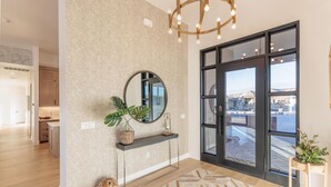 Un intérieur moderne avec un grand miroir, une console, un tapis à motifs et une vue à travers une porte vitrée.
