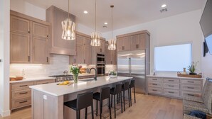 Une cuisine moderne avec des meubles en bois, des appareils en acier inoxydable, un îlot central doté de tabourets et un éclairage suspendu.