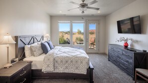 A bedroom with a bed, bedside tables, a dresser, a ceiling fan, and a TV on the wall. - 1 Top Ledge (St. George)