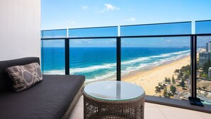 Un balcon avec vue sur l’océan et la plage, un canapé et une table en verre.