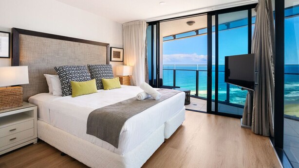 Une chambre d’hôtel moderne dotée d’un grand lit, d’une télévision et d’un balcon offrant une vue sur l’océan.