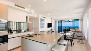 Une cuisine moderne dotée d’un îlot central, un coin repas avec vue et un espace de vie comprenant un canapé et des fauteuils.